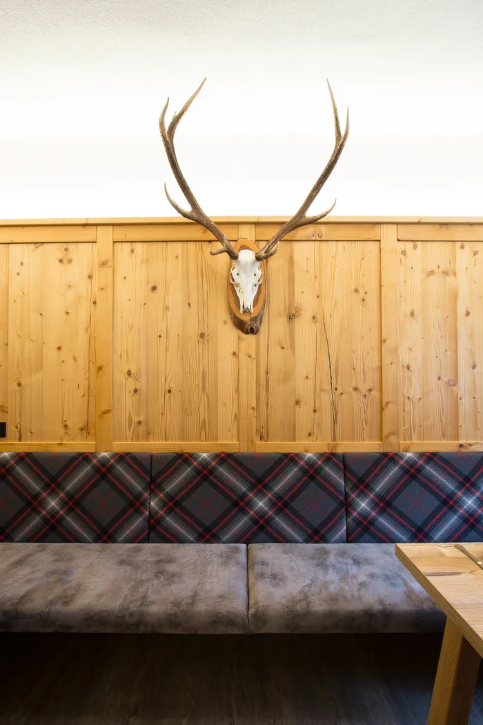 Gemütliche Sitzbank mit Karomuster vor Holzverkleidung und Hirschgeweih an der Wand