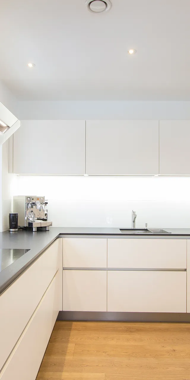 Moderne weiße Einbauküche mit Kochfeld, Dunstabzugshaube und Holzfußboden