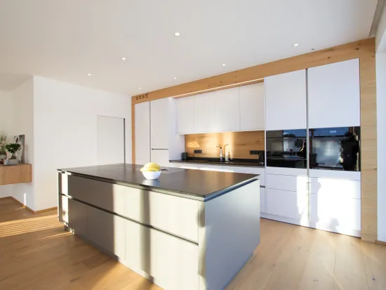 Moderne weiße Einbauküche mit Kochinsel, Holzverkleidung und natürlichem Lichteinfall