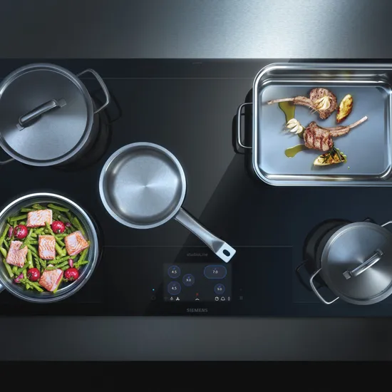 Moderne Siemens Induktionskochplatte mit mehreren Töpfen und Pfannen beim Kochen