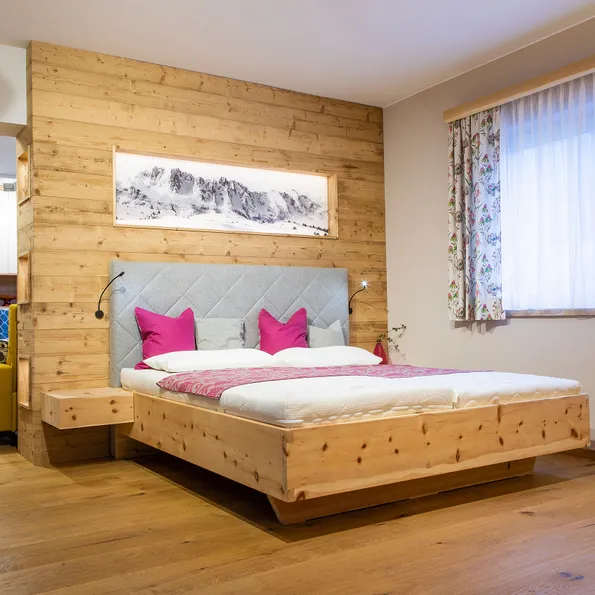 Modernes Schlafzimmer mit Holzbett, grauem Kopfteil und pinken Kissen im alpinen Stil