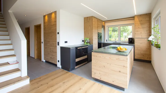 Moderne Küche mit Holzverkleidung, Kochinsel und großen Fenstern mit Gartenblick