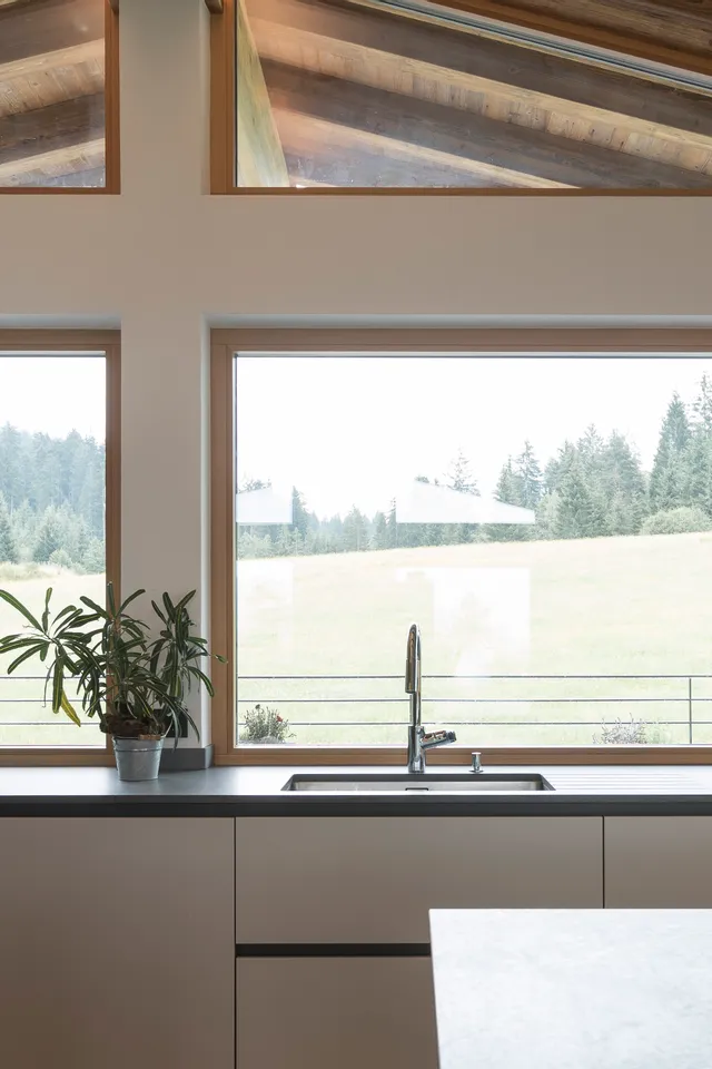 Moderne Küche mit schwarzer Einbauküche und großem Fenster mit Blick auf eine Waldwiese