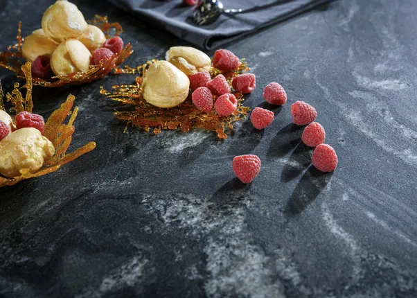 Dessert mit Brandteigkugeln, Himbeeren und Karamell auf dunkler Küchenarbeitsplatte