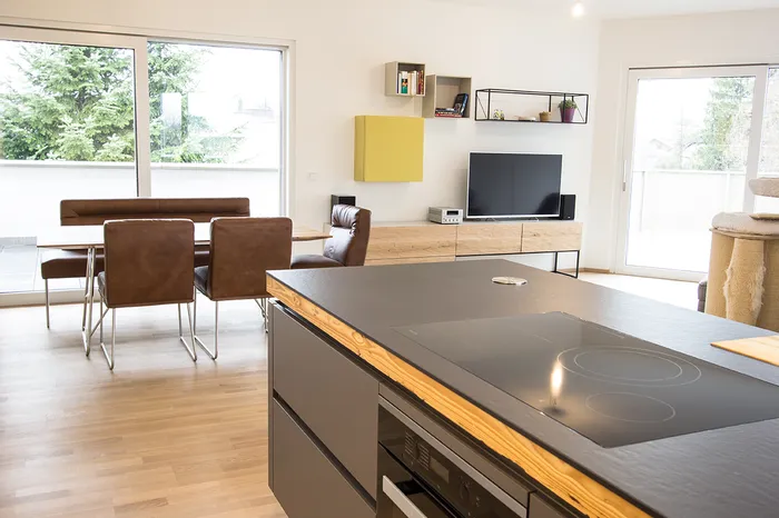 Moderne offene Wohnküche mit Kochinsel, Esstisch und Fernseher im hellen Raum