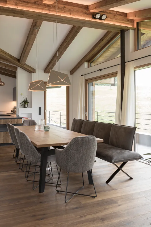 Moderne Wohnküche mit Holzboden, Sichtbalken, Essbereich und großen Fenstern mit Blick ins Grüne