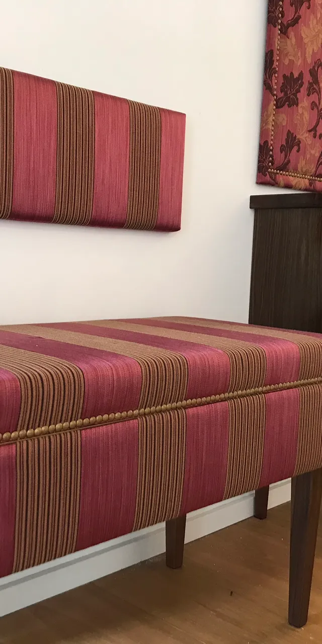 Gepolsterte Sitzbank mit rot-goldenen Streifen neben dunkler Holzkommode im Flur