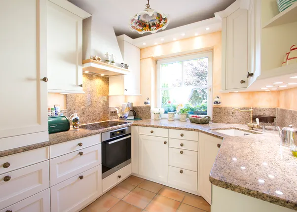 Helle Landhausküche mit Granit-Arbeitsplatten, weißen Schränken und Blick auf Garten durch Fenster