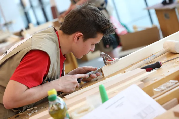 Junger Handwerker arbeitet konzentriert mit einem Stechbeitel an einem Holzstück in der Werkstatt