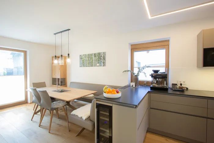 Moderne Wohnküche mit Esstisch aus Holz, grauen Stühlen und Obstschale auf Kücheninsel