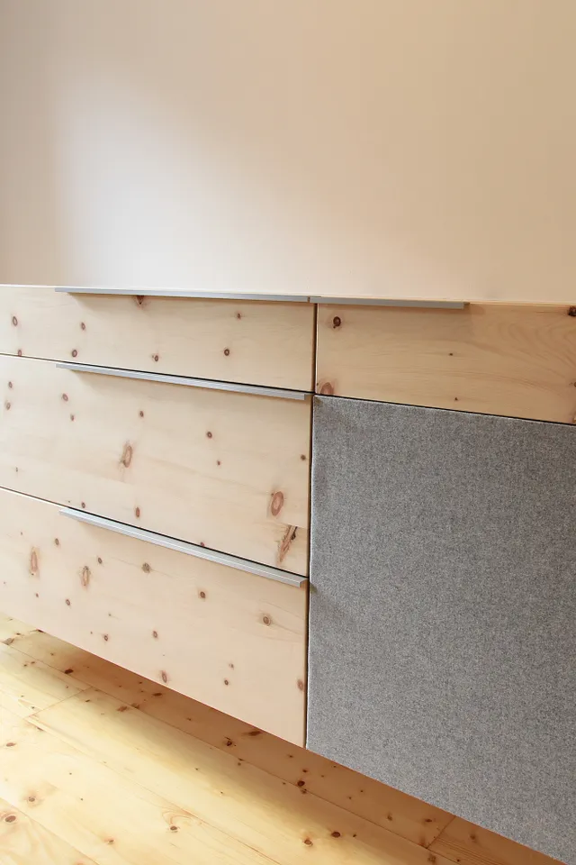 Moderne Hängeschrankkommode aus hellem Holz mit grauer Stofftür in minimalistischem Raum