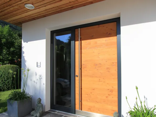 Moderne Haustür aus Holz mit Glasrahmen, flankiert von Pflanzen und Buddha-Statuen