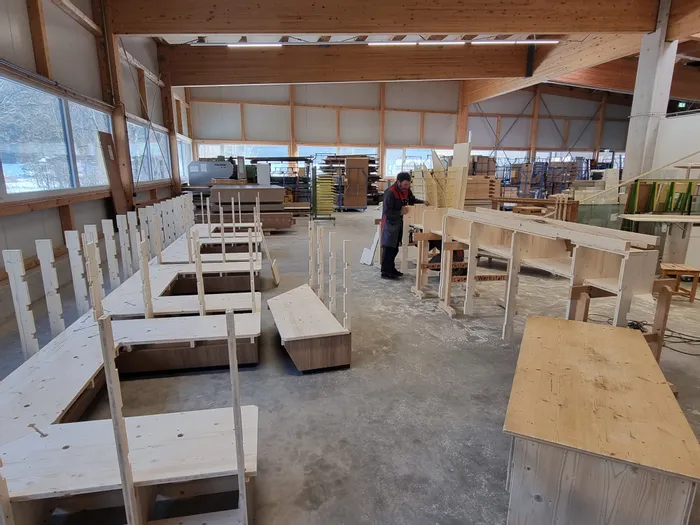 Tischler arbeitet in heller Werkstatt an Holzregalen und Möbelteilen aus hellem Holz