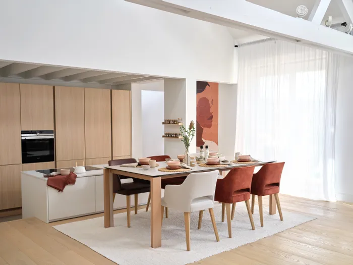 Modernes Esszimmer mit gedecktem Holztisch, gepolsterten Stühlen und offener Küche im Hintergrund