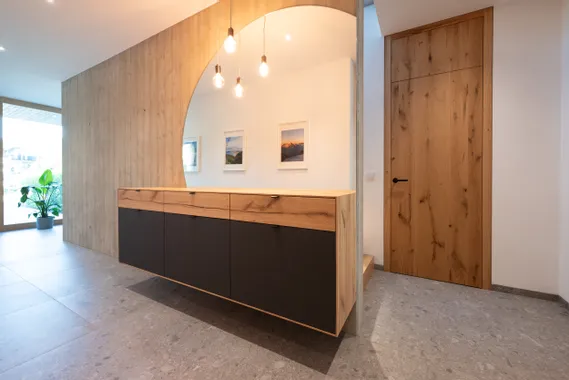 Moderner Flur mit Holz-Kommode, großem Spiegel, Designerlampen und Holztür auf Steinboden