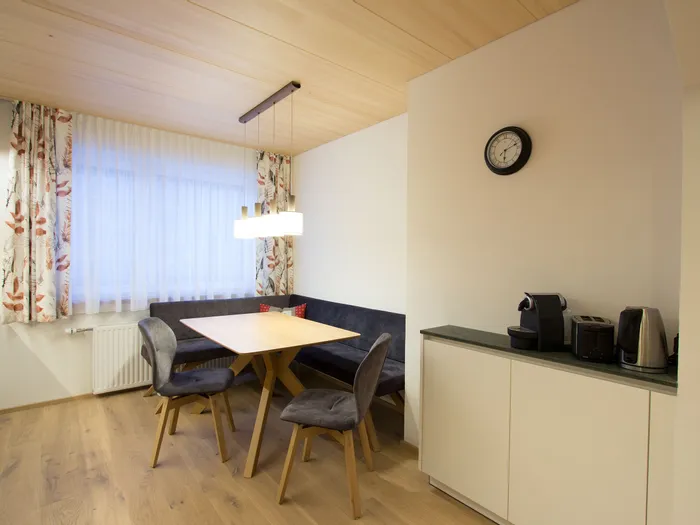 Moderne Essecke mit Holztisch, gepolsterter Sitzbank und Kaffeemaschine auf weißer Anrichte