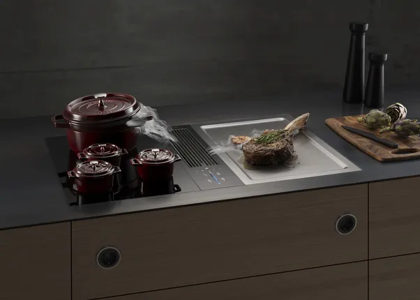 Moderne Kochstelle mit integriertem Dunstabzug, Gusseisentöpfen und Steak auf Grillfläche
