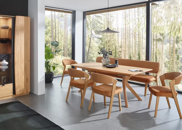 Modernes Esszimmer mit Holztisch, orange gepolsterten Stühlen und großem Fenster mit Waldblick