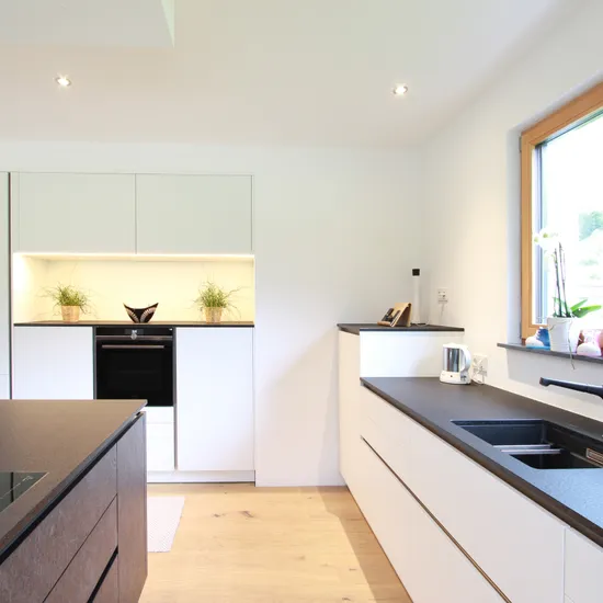 Moderne weiße Einbauküche mit schwarzer Arbeitsplatte und großem Fenster