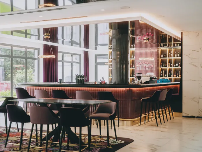 Moderne Hotelbar mit violetten Stühlen, beleuchtetem Tresen und Flaschenregalen im Hintergrund