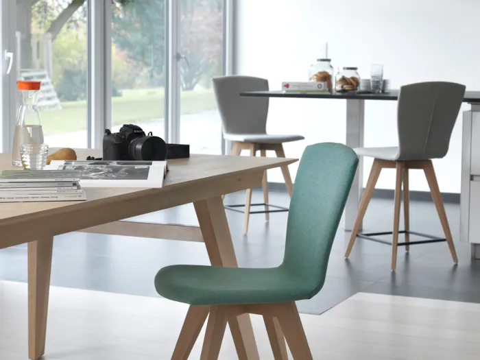 Moderner Esszimmerstuhl mit grünem Polster und Holzbeinen in einem hellen Wohnraum