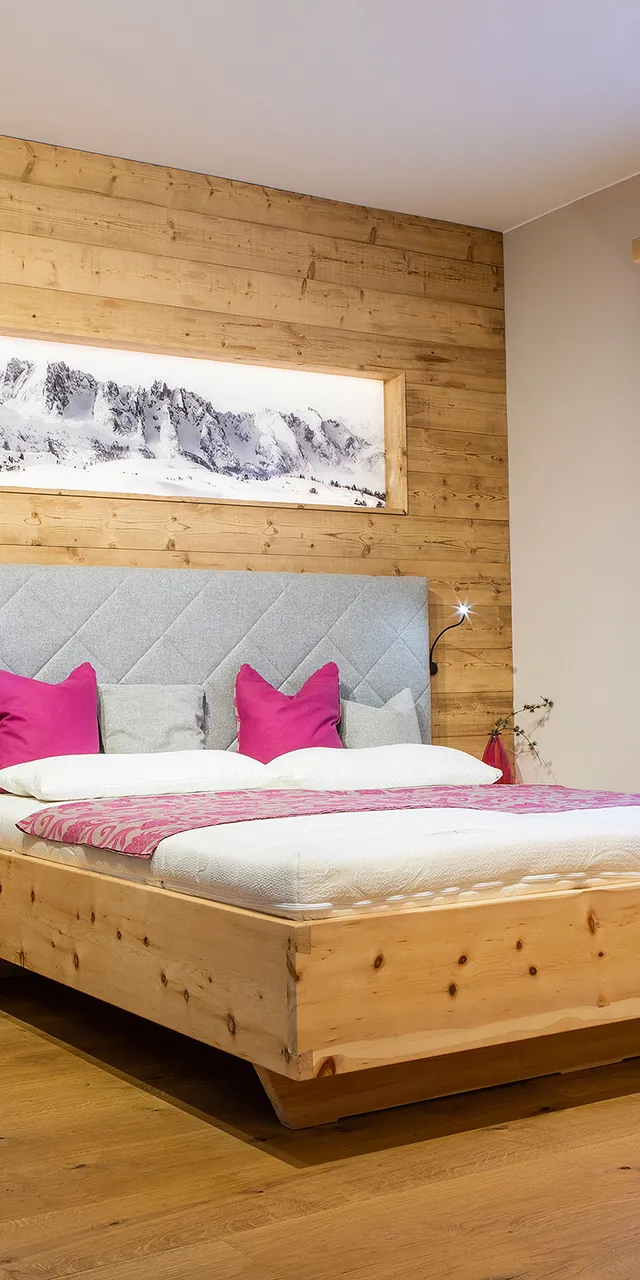 Modernes Schlafzimmer mit Holzbett, grauem Kopfteil und pinken Kissen im alpinen Stil