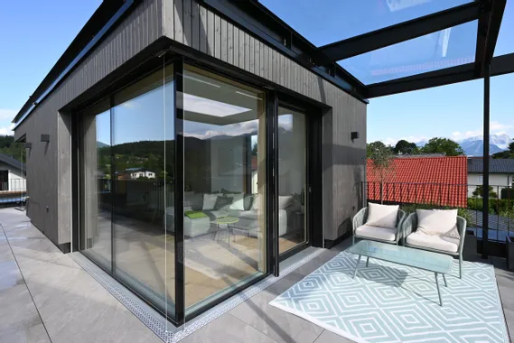 Moderne Terrasse mit Glasüberdachung, gemütlichen Sitzmöbeln und Panoramablick auf die Berge