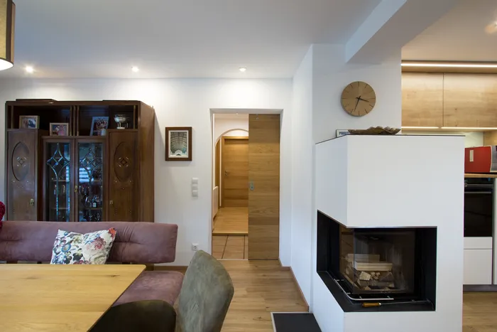 Modernes Wohnzimmer mit Kamin, Holzschrank, Esstisch und offener Tür zum Flur