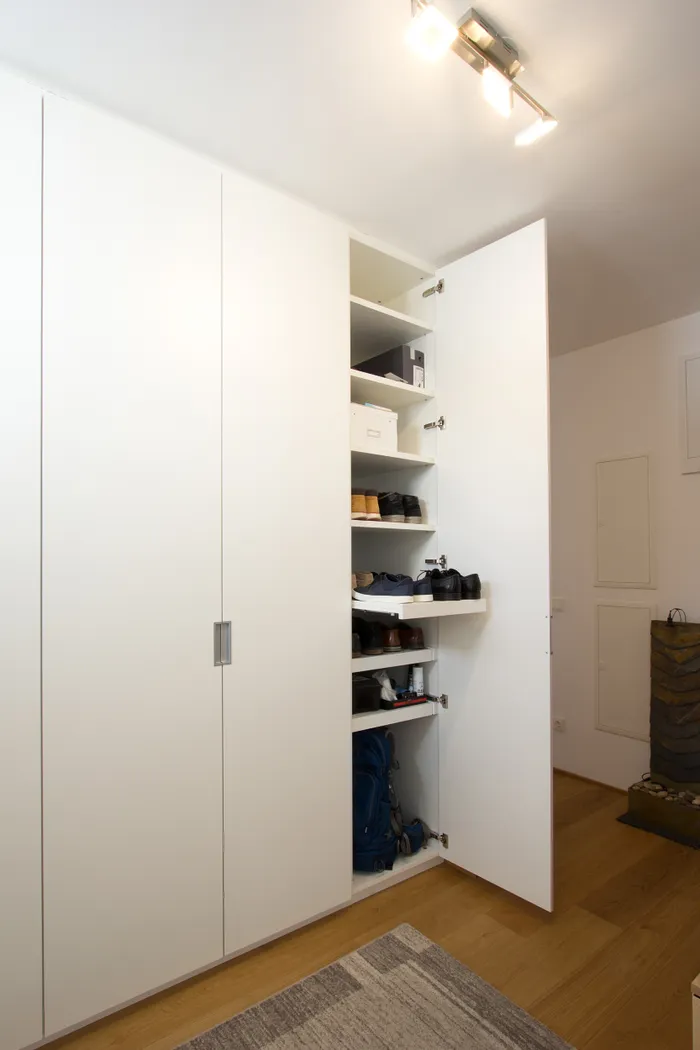 Geöffneter weißer Einbauschrank mit Regalen voller Schuhe und Aufbewahrungsboxen