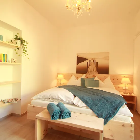 Helles Schlafzimmer mit Holzbett, blauer Decke, Nachttischen und Regalwand