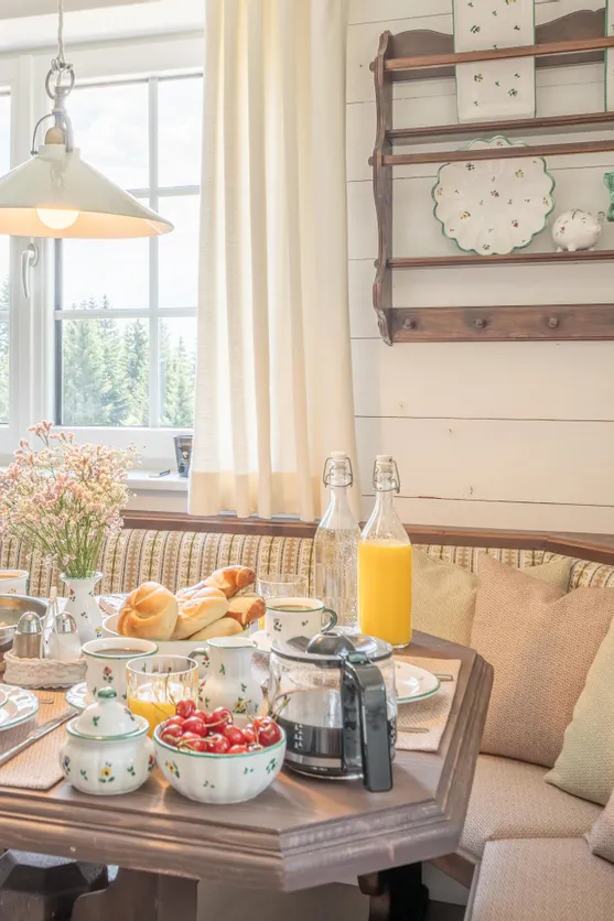 Gemütlicher Frühstückstisch mit Brötchen, Eiern, Saft und Blumen in einer Landhausküche