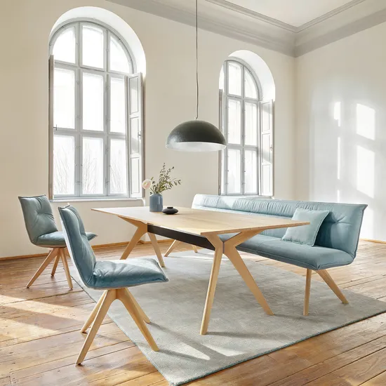 Helles Esszimmer mit Holztisch, blauen Polsterstühlen und großem Bogenfenster