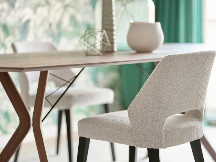 Modernes Esszimmer mit hellen Polsterstühlen und Holztisch vor tropischer Tapete