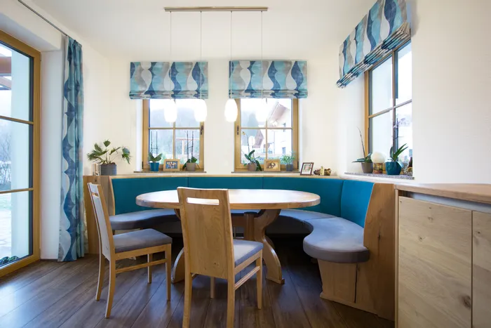 Gemütliche Essecke mit rundem Holztisch, blauer Polsterbank und Holzboden im modernen Landhausstil