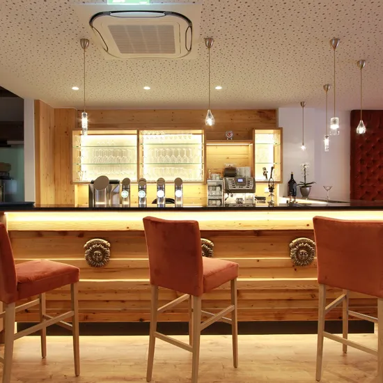 Moderne Hotelbar mit Holztheke, Barhockern und stilvoller Beleuchtung