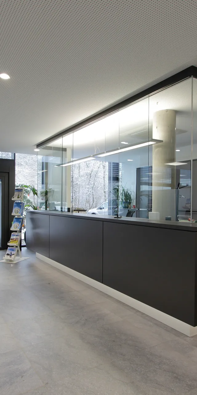 Moderne Empfangshalle mit schwarzem Tresen, Glaswänden und Prospektständern bei Tageslicht