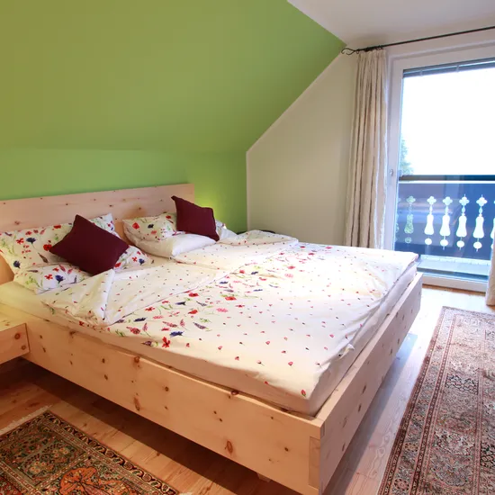 Helles Schlafzimmer mit Doppelbett aus Holz, Bettwäsche mit Blumenmuster und Zugang zum Balkon