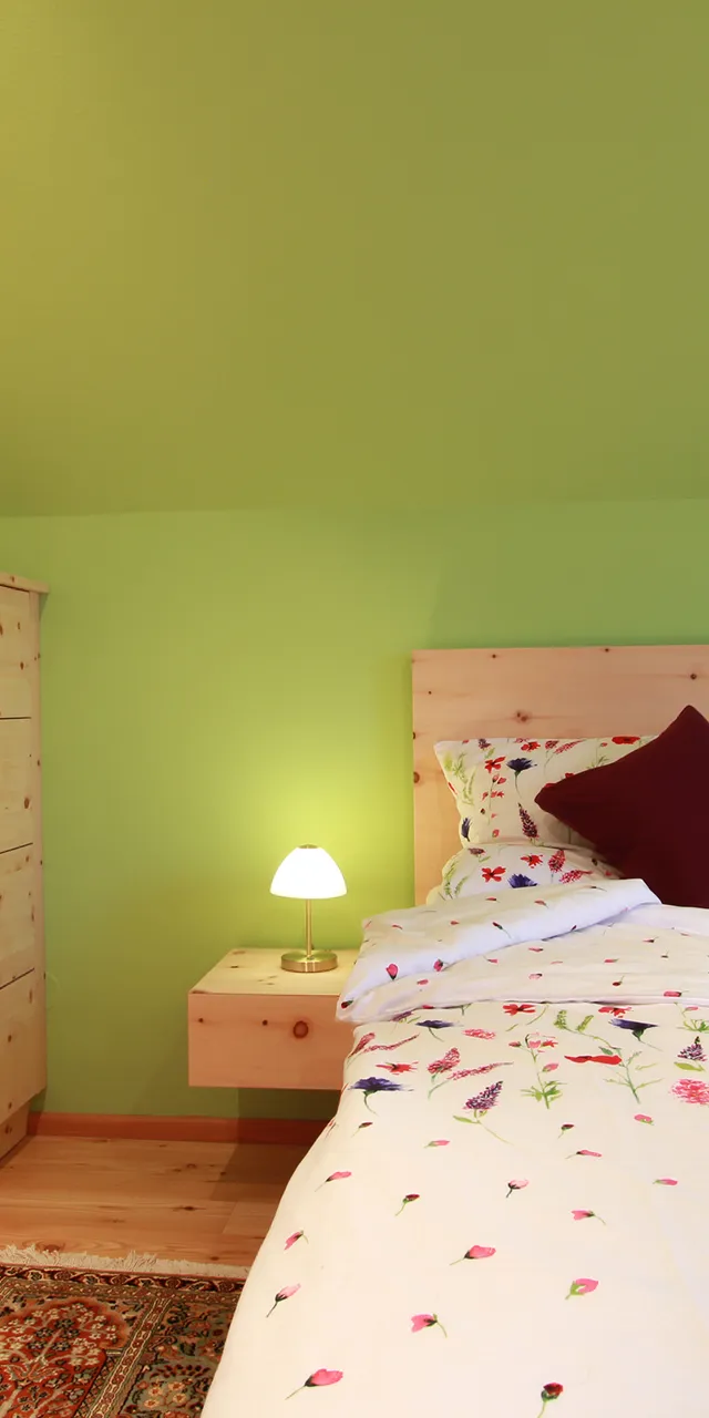 Gemütliches Schlafzimmer mit Holzbettrahmen, grüner Wandfarbe und floraler Bettwäsche