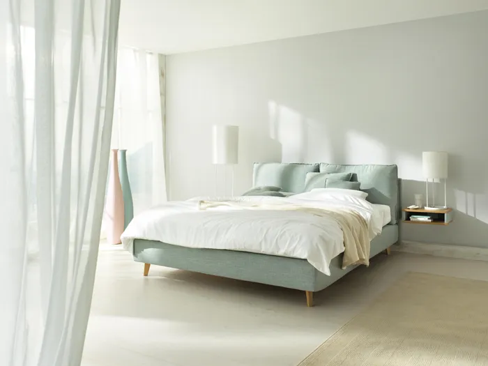 Modernes Schlafzimmer mit hellblauem Polsterbett und natürlichem Lichteinfall