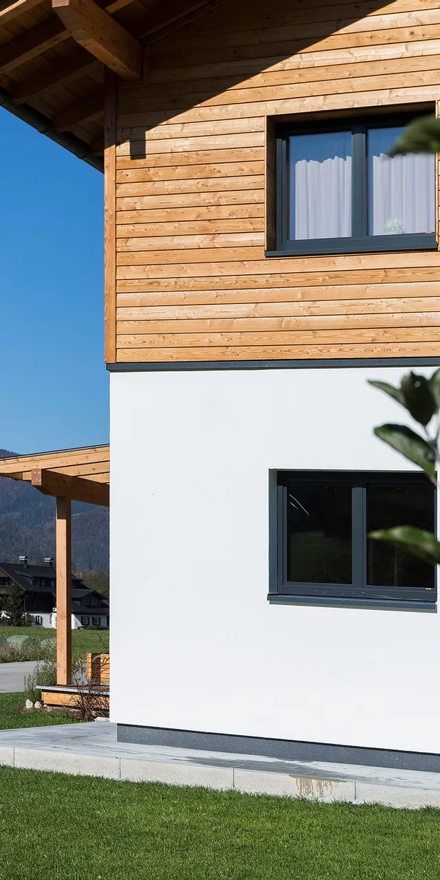 Modernes Holzhaus am Stadtrand mit Alpenblick und grüner Wiese im Vordergrund