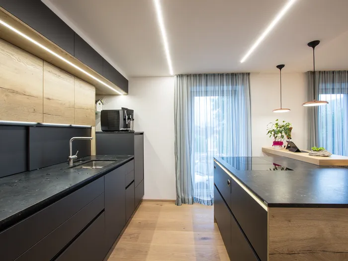 Moderne Küche mit schwarzen Schränken, Holzdetails und Kücheninsel mit Induktionskochfeld