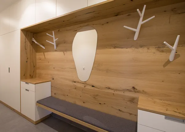 Moderner Garderobenbereich mit Holzverkleidung, weißen Haken und Sitzbank
