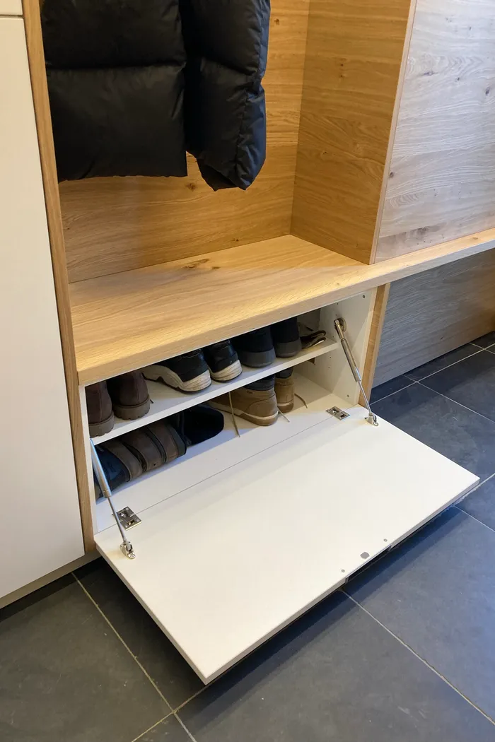 Offenes weißes Schuhregal mit mehreren Paar Schuhen in einer modernen Holzgarderobe