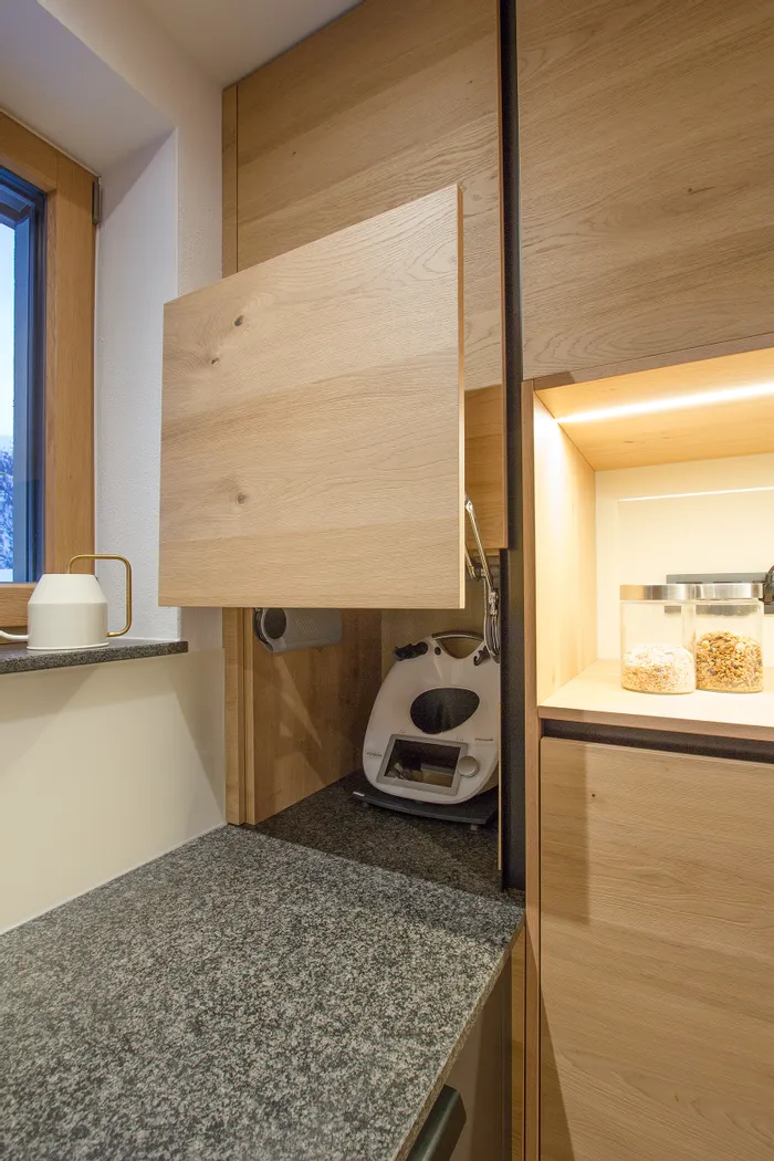 Küchengerät in einem eingebauten Holzschrank mit offener Frontklappe neben Vorratsgläsern