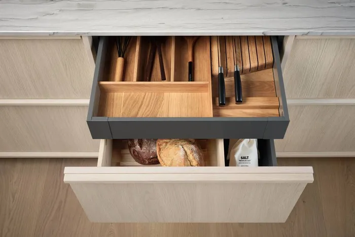Geöffnete Küchenschubladen mit Holzbesteckeinsatz, Messern, Brot und Salzpackung