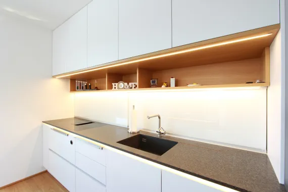 Moderne weiße Einbauküche mit dunkler Arbeitsplatte und LED-Unterbauleuchten