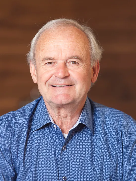 Älterer Mann mit grauen Haaren und blauem Hemd lächelt vor unscharfem Hintergrund
