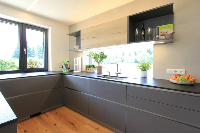 Moderne Küche mit grauen Schränken, Obstschale, Küchenmaschinen und Kräutertöpfen bei Tageslicht