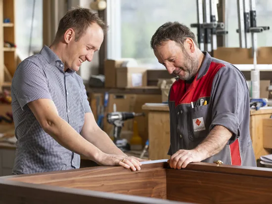 Zwei Männer begutachten gemeinsam ein Holzprojekt in einer Tischlerwerkstatt