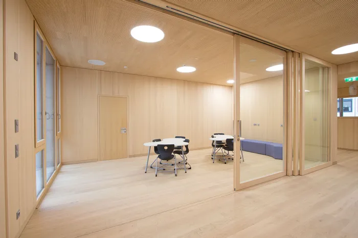 Moderner Lernraum mit Holzwänden, runden Tischen und schwarzen Stühlen